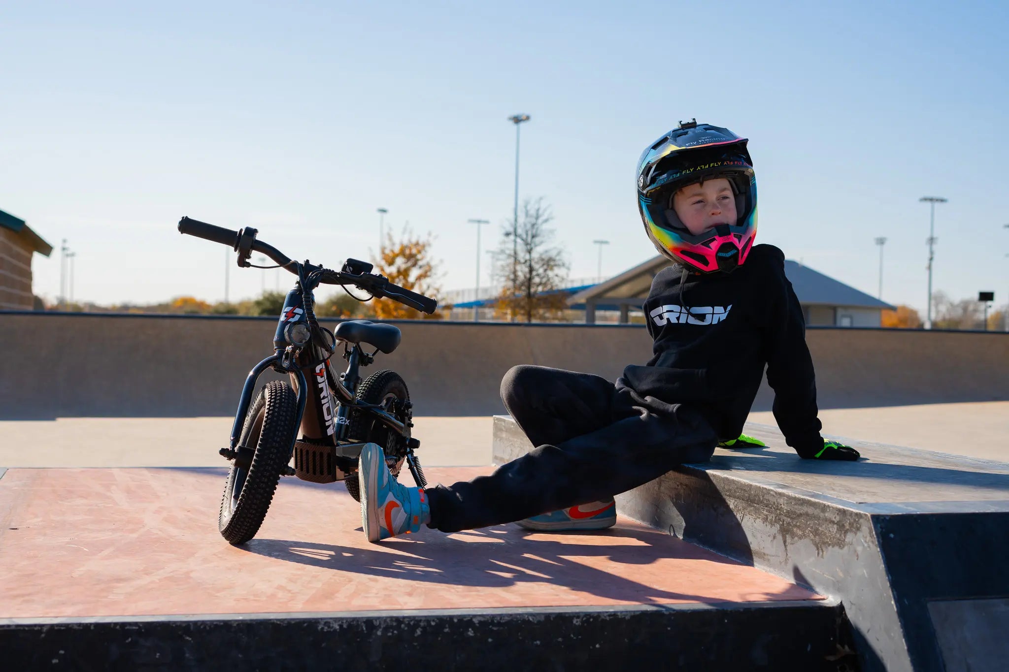 Young Orion rider resting beside an electric balance bike at a skate park