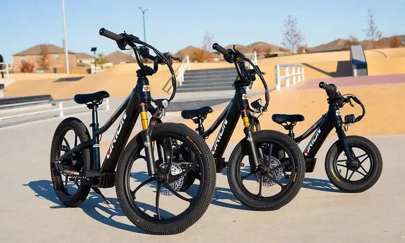 Three black electric bikes parked on a concrete surface with a clear sky.